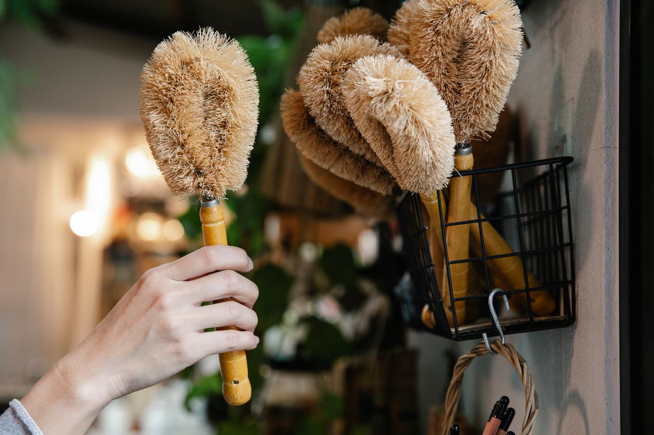 services-01 Close-up of a hand selecting eco-friendly cleaning brushes from a basket indoors.